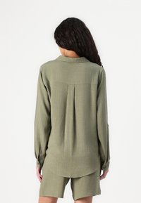 Groene, lange mouwen shirt met een plooi aan de achterkant, knopen manchetten en een gebogen zoom, gemaakt van een gestructureerde stof, gecombineerd met bijpassende shorts.