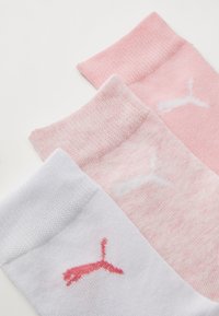 Tre par med sokker: en hvit, en lys rosa, en rosa. Hver har en stripete mansjett og en logo brodert i kontrastfarger.