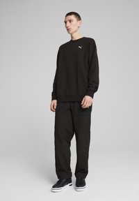 Sudadera negra con cuello redondo y logo bordado, combinada con pantalones cargo negros de corte holgado y zapatillas negras.