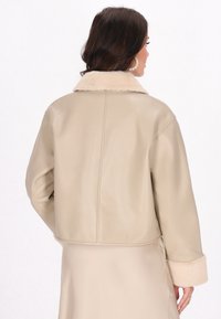 Beige Lederjacke mit einem weichen Pelzkragen. Verfügt über ein cropped Design, lange Ärmel und mit Pelz gefütterte Manschetten. Glatte Textur mit minimaler Verzierung.