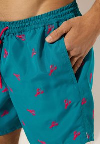 Bermuda de bain teal avec un cordon de serrage à la taille, ornée de motifs de homard brodés rouges, et dotée de poches latérales pour plus de commodité.