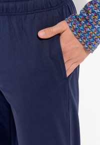 Navy blue sweatpants with an elastic waistband and side pocket, paired with a multicolored zigzag patterned shirt cuff.