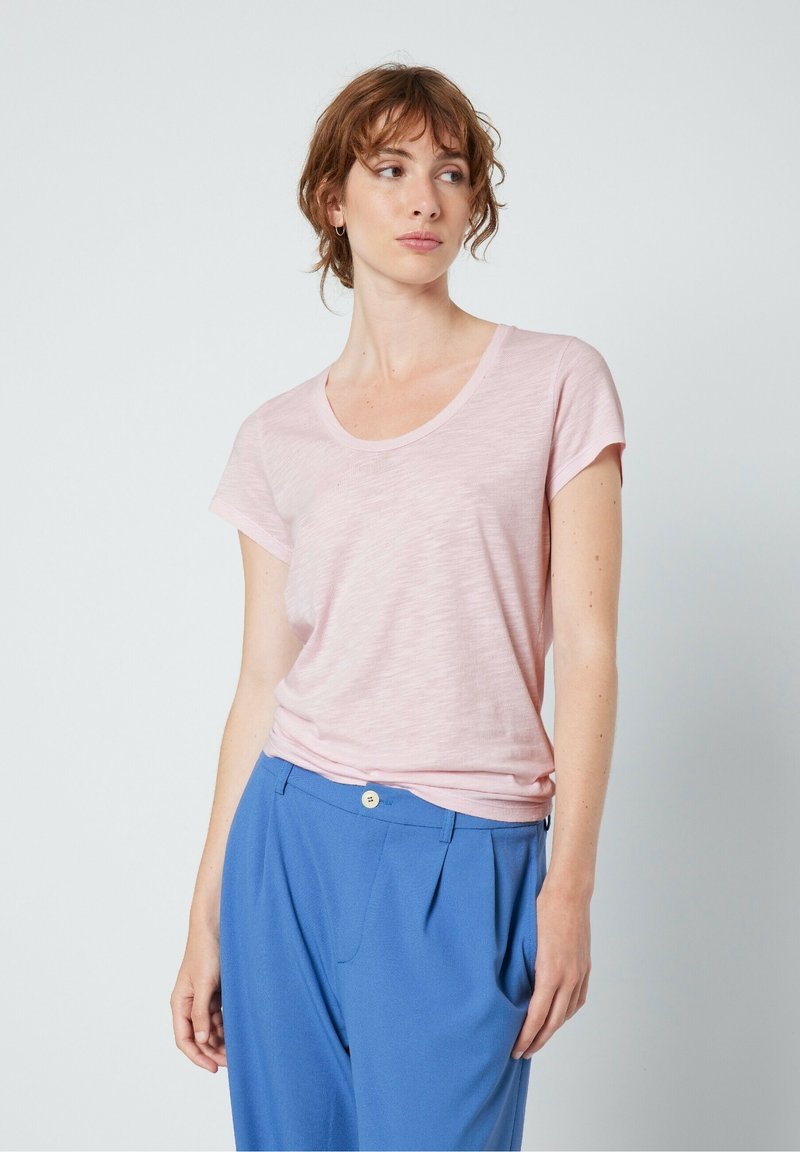 Gaiši rozā īsām piedurknēm T-krekls ar apaļu kakla izgriezumu, izgatavots no mīkstas auduma, kombinēts ar zilām krokām biksēm. Vienkāršs, brīvs piegriezuma dizains.