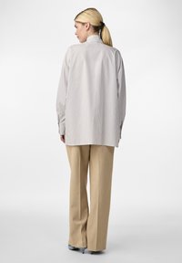 Chemise rayée gris clair avec une coupe décontractée, manches longues et poignets boutonnés, associée à un pantalon large beige et des chaussures à talons.