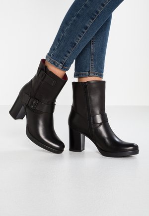 Black leather ankle boots with a round toe, high block heel, side zip, and decorative buckle strap. Smooth texture with a glossy finish.