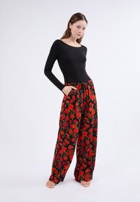Blusa negra de manga larga combinada con pantalones negros fluidos con un patrón floral rojo. Los pantalones tienen una cintura elástica y bolsillos.