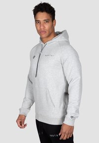Gray pullover hoodie with a front pocket, adjustable neckline, and contrasting black logo detail on the chest and sleeve. Soft fabric texture.