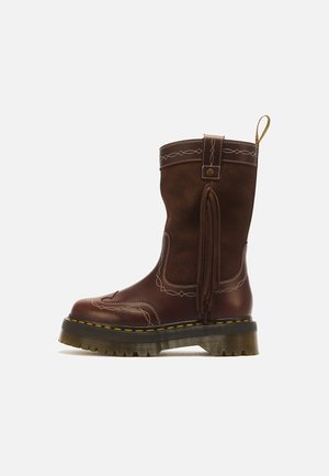 Botte mi-mollet en cuir et daim marron foncé avec semelle épaisse à rainures, coutures décoratives blanches et détail de franges latérales sur fond uni.