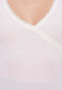 Top bianco a coste con scollatura a V e bordo in pizzo lungo il collo, caratterizzato da una texture morbida e un design aderente.