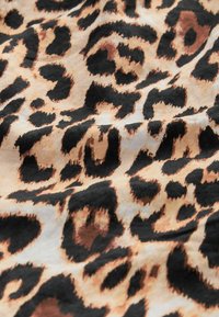 Gros plan sur un tissu avec un motif léopard dans des tons marron, beige et noir, montrant la texture et de légères rides.