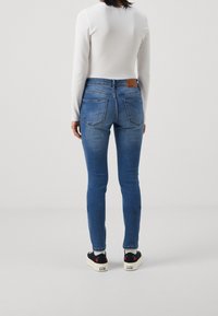 Hubené modré džíny s středním pasem, pěti kapsami a hnědou koženou nášivkou na zadní straně. Kombinované s černými teniskami.