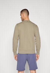 Olive green sweatshirt with long sleeves and ribbed cuffs, paired with purple shorts. Features a round neckline and a small back logo detail.