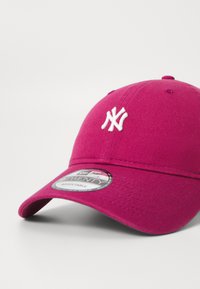 Rózsaszín baseball sapka fehér hímzett logóval. Gömbölyű napellenzővel és állítható pánttal rendelkezik. Texturált anyag, sima felülettel.