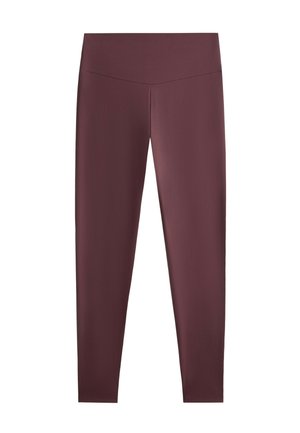 Femme portant de grandes lunettes de soleil noires, une veste crème, une chemise rayée, des leggings bordeaux, des chaussettes blanches, des baskets et portant un sac crème sur fond gris.