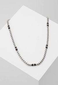 Collier en chaîne argentée avec des segments noirs dispersés. Les maillons sont texturés, offrant un mélange de finitions brillantes et mates.
