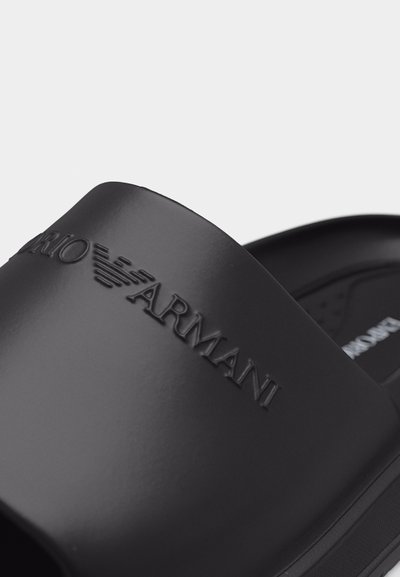 Μαύρο σανδάλι slide με ανάγλυφο το λογότυπο Emporio Armani στο λουρί, διαθέτει υφασμένο πέλμα και κομψό, μινιμαλιστικό σχεδιασμό.