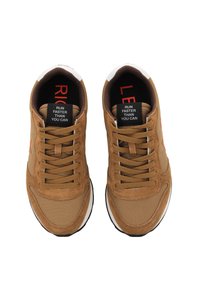 Scarpe sportive marroni con un mix di materiali in suede e tessuto, chiusura con lacci e suole in gomma bianca con testo rosso su etichette nere.