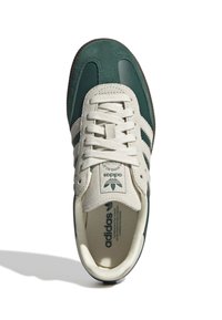 Grön och gräddfärgad sneaker i mocka och läder, med tre vita ränder, rund tå och en texturerad brun gummisula.