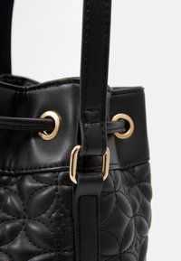 Czarna skórzana torba typu bucket z pikowanym wzorem, złotymi akcentami i regulowanym paskiem o gładkiej fakturze.