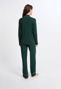 Grön långärmad pyjamas med vit piping. Överdelens har en krage och rundad nederkant, medan byxorna är raka med en avslappnad passform.