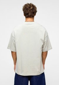T-shirt oversized gris clair avec des manches courtes, encolure ronde, texture douce et ourlet droit. Détails de couture visibles le long des bords.