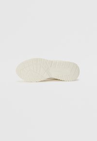Sneaker sole in off-white rubber with textured pattern, including traction lugs and grooves for grip and flexibility.