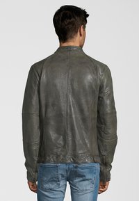 Šedá kožená bunda s hladkým povrchem, přiléhavým střihem a minimálním zdobením. Pohled zezadu ukazuje švy na ramenou a rovný střih.