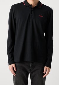 Schwarzes Langarm-Polohemd mit einem kontrastierenden roten Kragen und besticktem Logo. Hergestellt aus weichem Stoff, mit schmaler Passform und Knopfleiste.