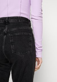 Svart högmidjade jeans i en texturerad tygkvalitet med kontrasterande sömmar. Har två bakfickor och en etikett på midjebandet.