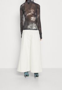 Musta pitkähihainen paita, jossa on sitruunakuvio, yhdistettynä valkoiseen pitkähihaiseen, leveälahkeiseen farkkuhameeseen. Näkyvät siniset korkokengät täydentävät asukokonaisuuden.