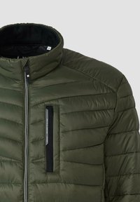 Grüne gepolsterte Jacke mit hohem Kragen. Verfügt über einen Front-Reißverschluss und eine Brusttasche mit schwarzem Akzent. Horizontale Nähte über den Stoff.