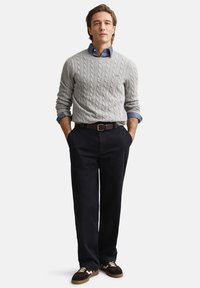 Siv pulover z rebrastim vzorcem čez modro srajco z ovratnikom, kombiniran z mornarsko modrimi hlačami in temnimi supergami, s rjavim pasom, ki pritiska pas.