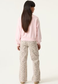 Mujer con cabello largo y oscuro de espaldas, vistiendo una sudadera rosa claro y pantalones anchos beige con estampado de leopardo.