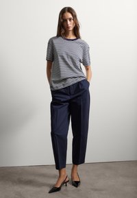 Camiseta de cuello redondo a rayas en navy y blanco, combinada con pantalones navy de cintura alta y zapatos de tacón kitten negros. Textura de tela suave.