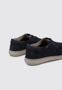 Baskets en daim bleu marine avec une finition texturée, dotées de semelles en caoutchouc beige en contraste et de lacets bleu marine. Branding minimal sur le côté.