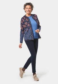 Gilet en maille navy avec des accents en corail et bleu, associé à un haut bleu clair, un pantalon sombre et des baskets beiges.