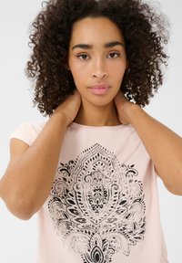 T-shirt rose clair avec un grand motif paisley noir. Tissu doux avec un col rond et des manches courtes.