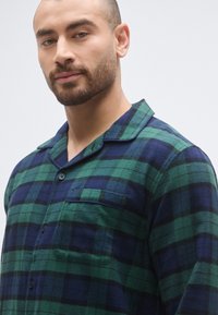 Zeleni i mornarskoplavi flanelasti pidžama gornji dio s ovratnikom s urezom, kopčanjem na gumbe i jednim džepom na prsima. Mekana tekstura, ležeran dizajn.