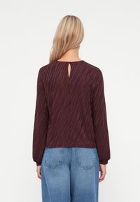 Langärmliges Top in Mauve mit einem strukturierten Tigerstreifenmuster, einem runden Halsausschnitt und einer Schlüssellochöffnung auf der Rückseite. Lässige Passform.