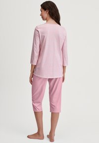 Roze geruite top met driekwartmouwen en ronde hals, gecombineerd met effen roze capri-broek. Gemaakt van zachte, lichte stof.