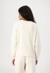 Cremefarvet sweater med et tekstureret strikdesign, rund hals og ribbede manchetter. Kombineret med lyse, højtaljede bukser.