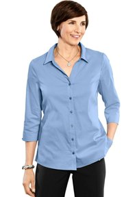 Camicia azzurra chiara con colletto, maniche a tre quarti e bottoni scuri. Texture del tessuto piatta, abbinata a pantaloni scuri.