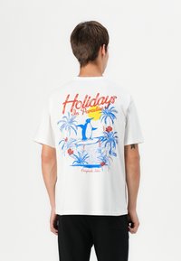 T-shirt bianca in cotone con una grafica colorata raffigurante un pinguino, palme e fiori sul retro. Maniche corte e vestibilità rilassata.