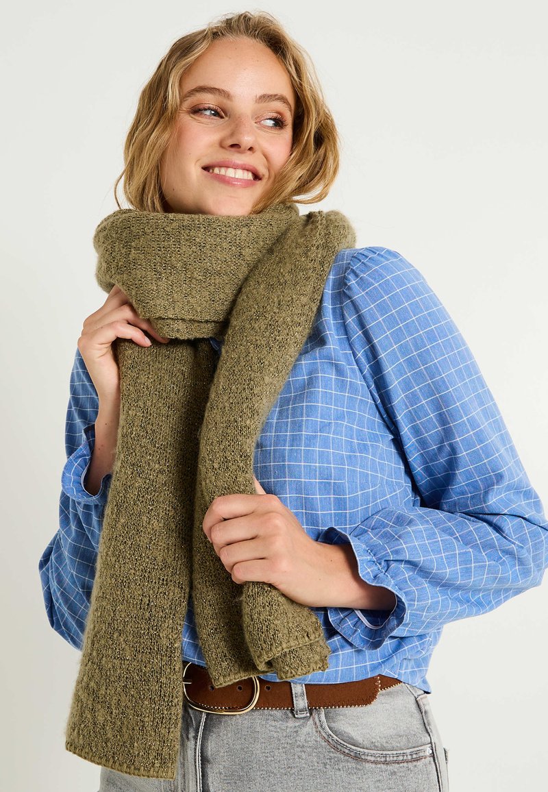 Écharpe en tricot vert olive, texture douce, finition légèrement duveteuse, tombe lâchement autour du cou, maintenue en sécurité, assortie à une chemise à carreaux bleue.