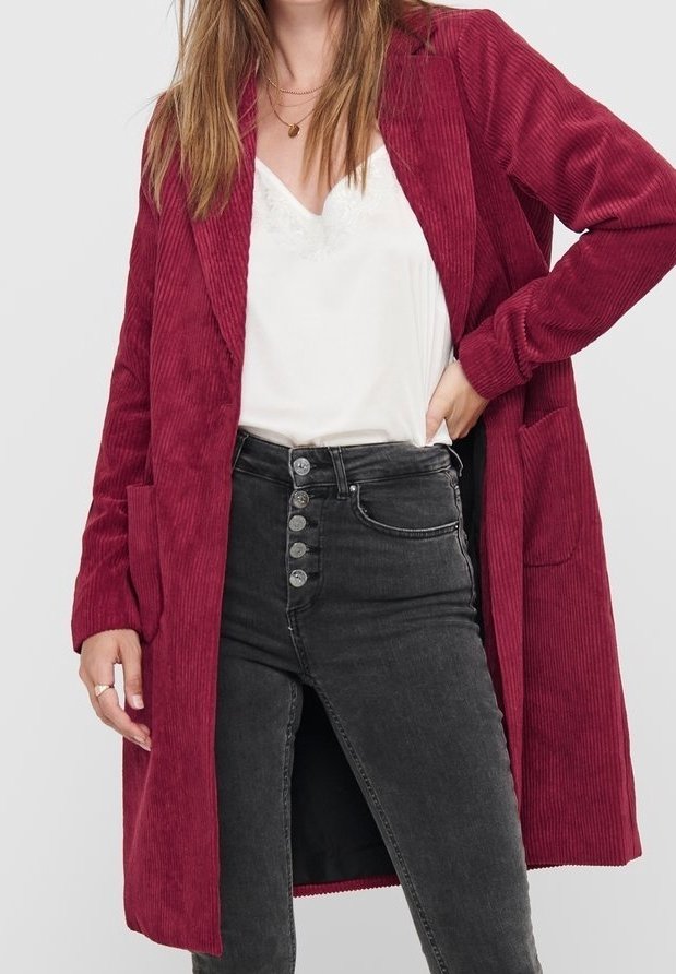 Abrigo de pana burdeos con manga larga, solapas con muesca y dos bolsillos delanteros, combinado con jeans negros de cintura alta y una blusa blanca.