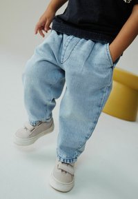 Vaaleansiniset farkut, joissa on rento malli, sivutaskut ja hillityt laskokset vyötäröllä, yhdistettynä beigeihin tarranauhakengiin.