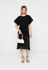 Svart kjole med korte, brede ermer og fransede kanter. Hvit håndveske med en buet design og svarte sandaler med remmer. Minimalistisk estetikk.