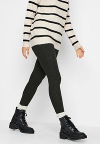 Leggings neri a coste abbinati a un maglione oversize a righe beige e nero, e stivali neri con lacci e suola spessa.