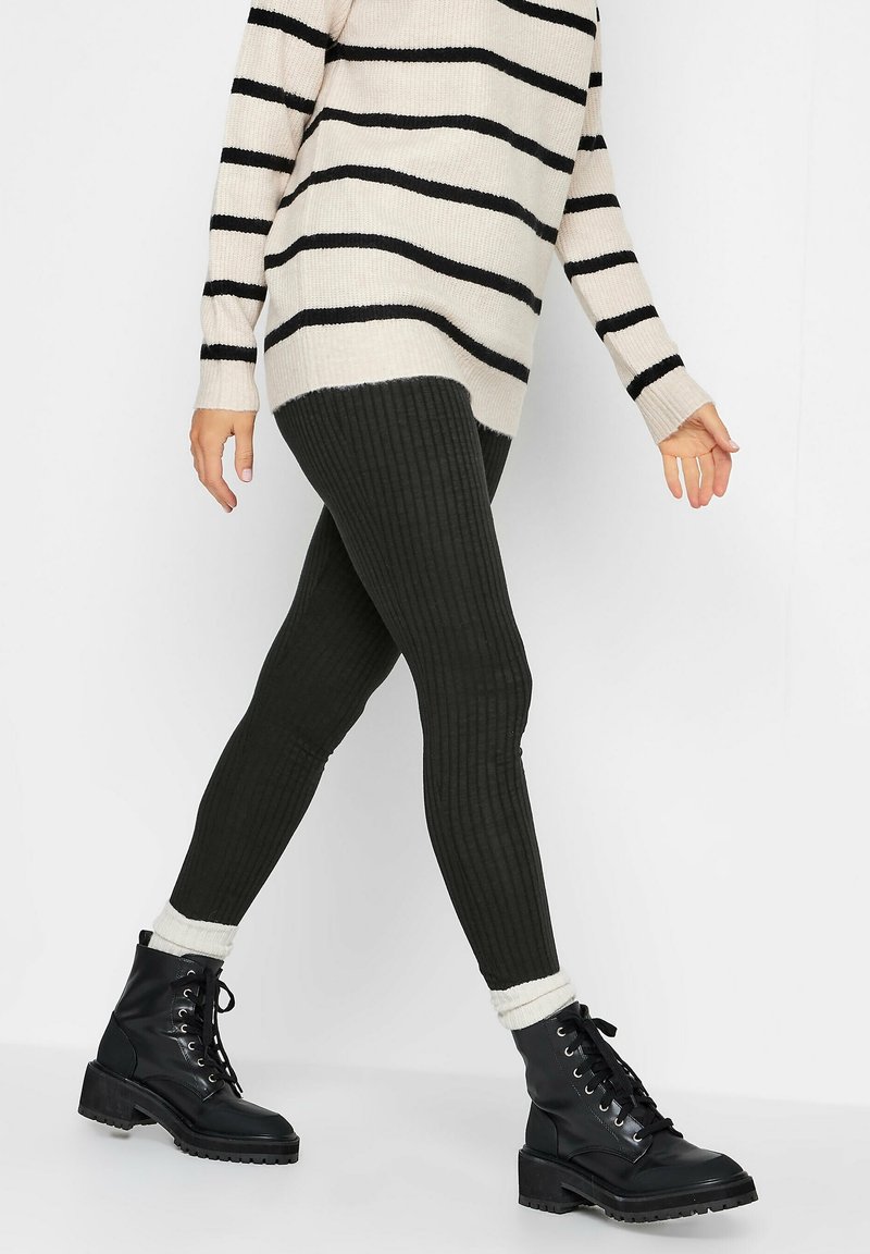 Leggings neri a coste abbinati a un maglione oversize a righe beige e nero, e stivali neri con lacci e suola spessa.