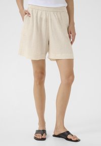 Shorts beige clair avec une ceinture élastique et des poches latérales. Fabriqués en tissu texturé, avec une coupe décontractée et une longueur mi-cuisse.